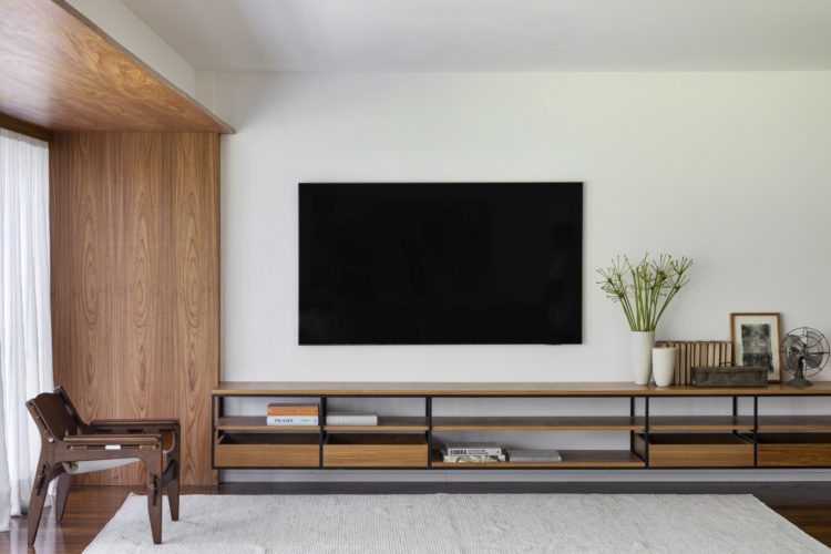 Espaço da tv na sala. Um rack com desenho limpo, em madeira e aço na cor preta, uma tapete cinza e só.
