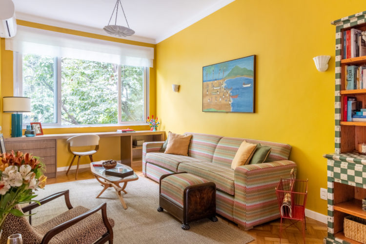 Sala com todas as paredes pintadas na cor amarelo ouro, sofá listrado, poltrona de onça