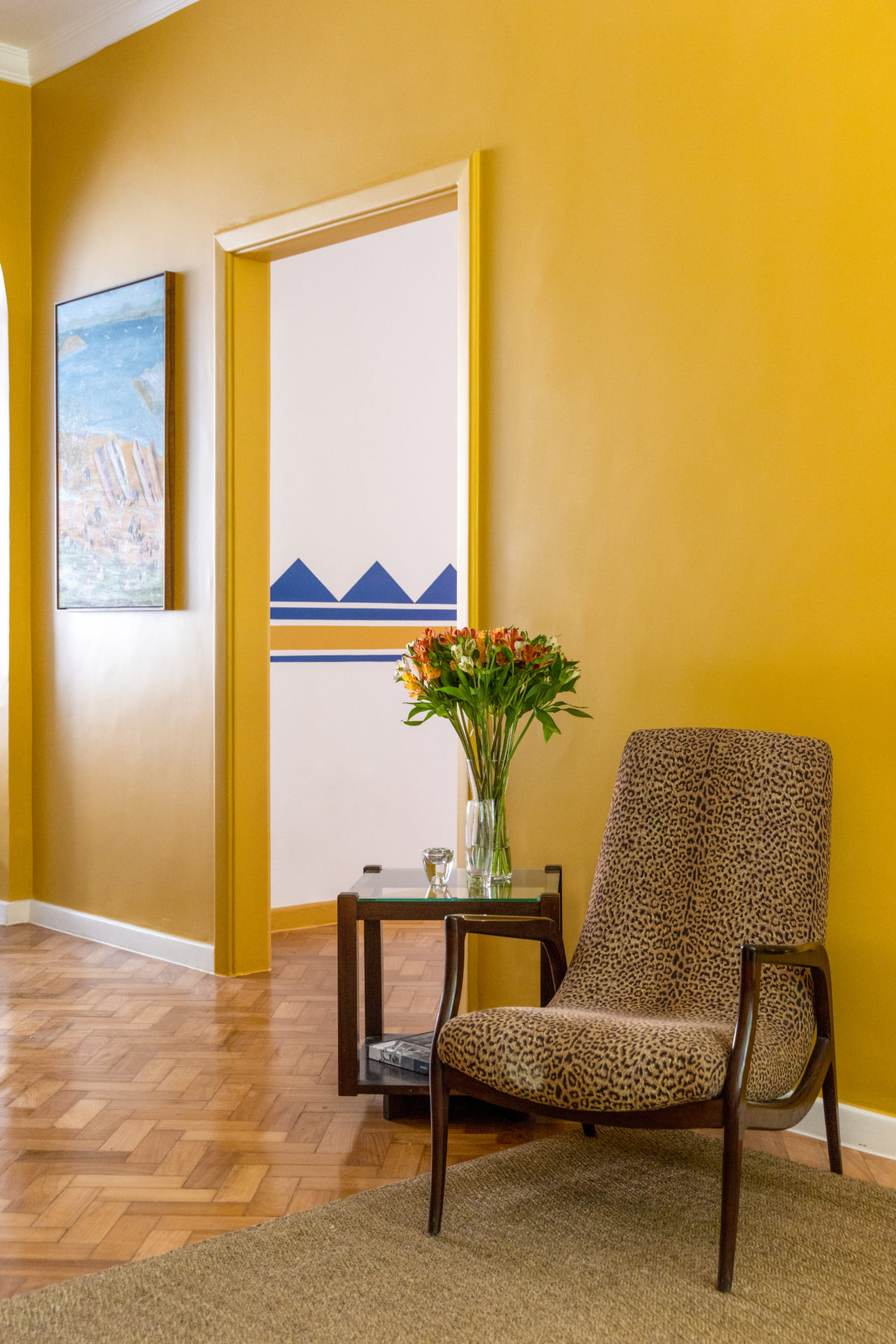 Um catinho da sala que tem a parede pintada de amarelo ouro, e uma poltrona estampada de onça
