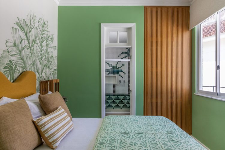 Quarto com as paredes verdes, e papel de parede branco e verde atras da cama