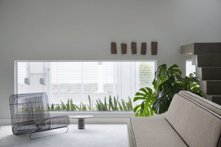 Casa decorada em estilo minimalista, com uma poltana em metal vazado e um sofá bege
