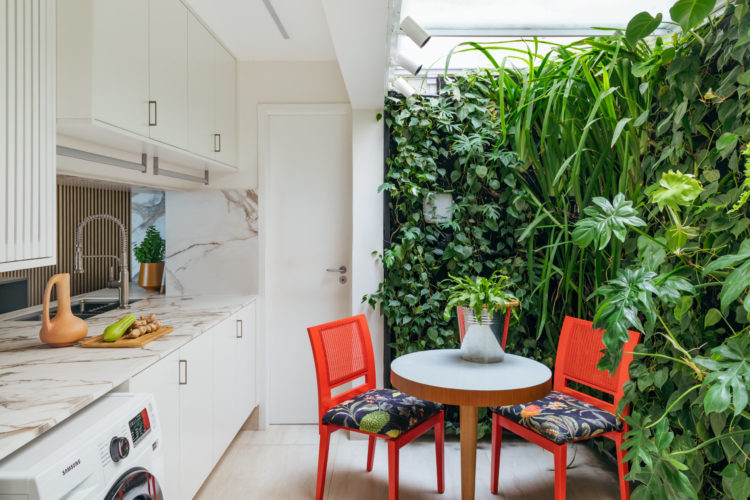 Espaço da cozinha e da área de serviço interligados, com um cantinho de parede verde, uma mesa redonad e duas cadeiras laranjas.