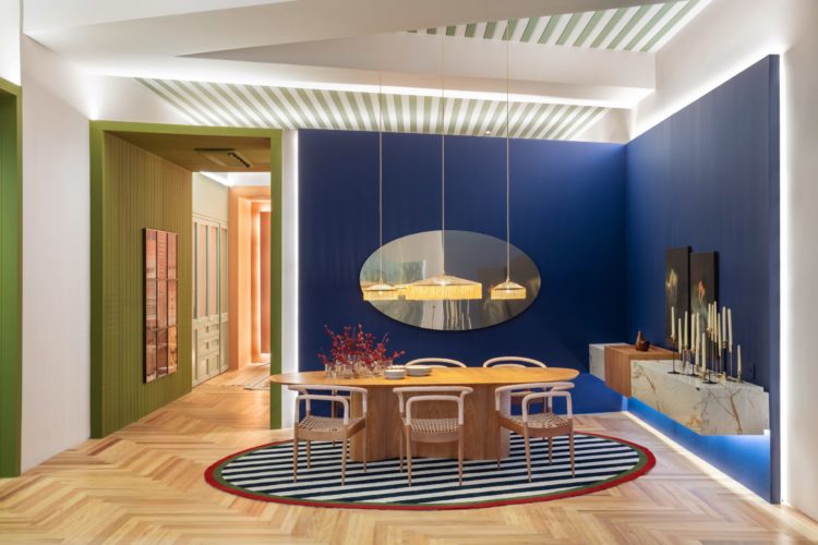 Cor é vida. Ambiente de mesa de jantar, com as paredes azuis ao fundo, teto listrado de branco e verde, tapete listrado