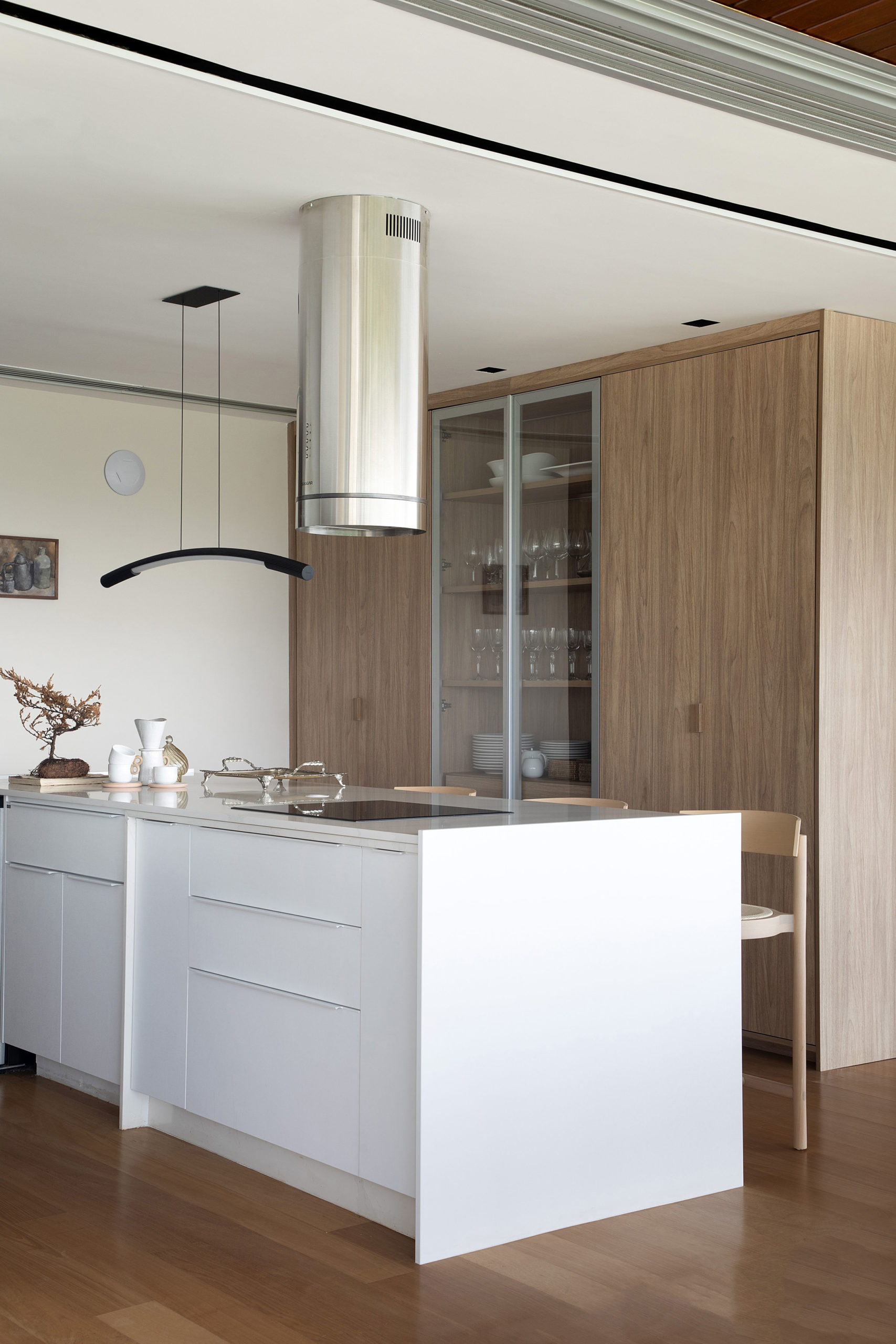 Cozinha incorporada ao living, com os armarios na cor branca, e ao fundo, um armario em madeira, com a porta do meio em vidro.
