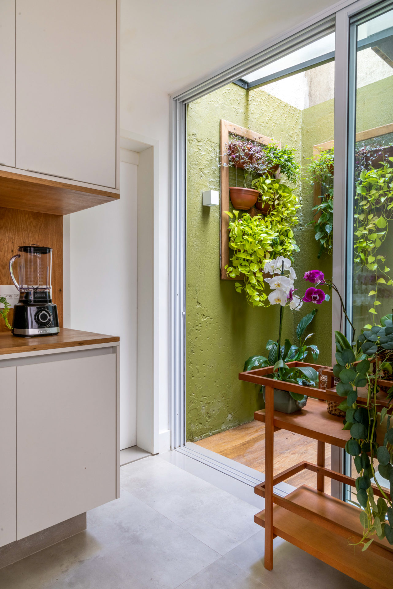 Ao lado da cozinha, um pequeno espaço aberto, sem teto, com muras pintados de verde e quadros com plantas penduradas.