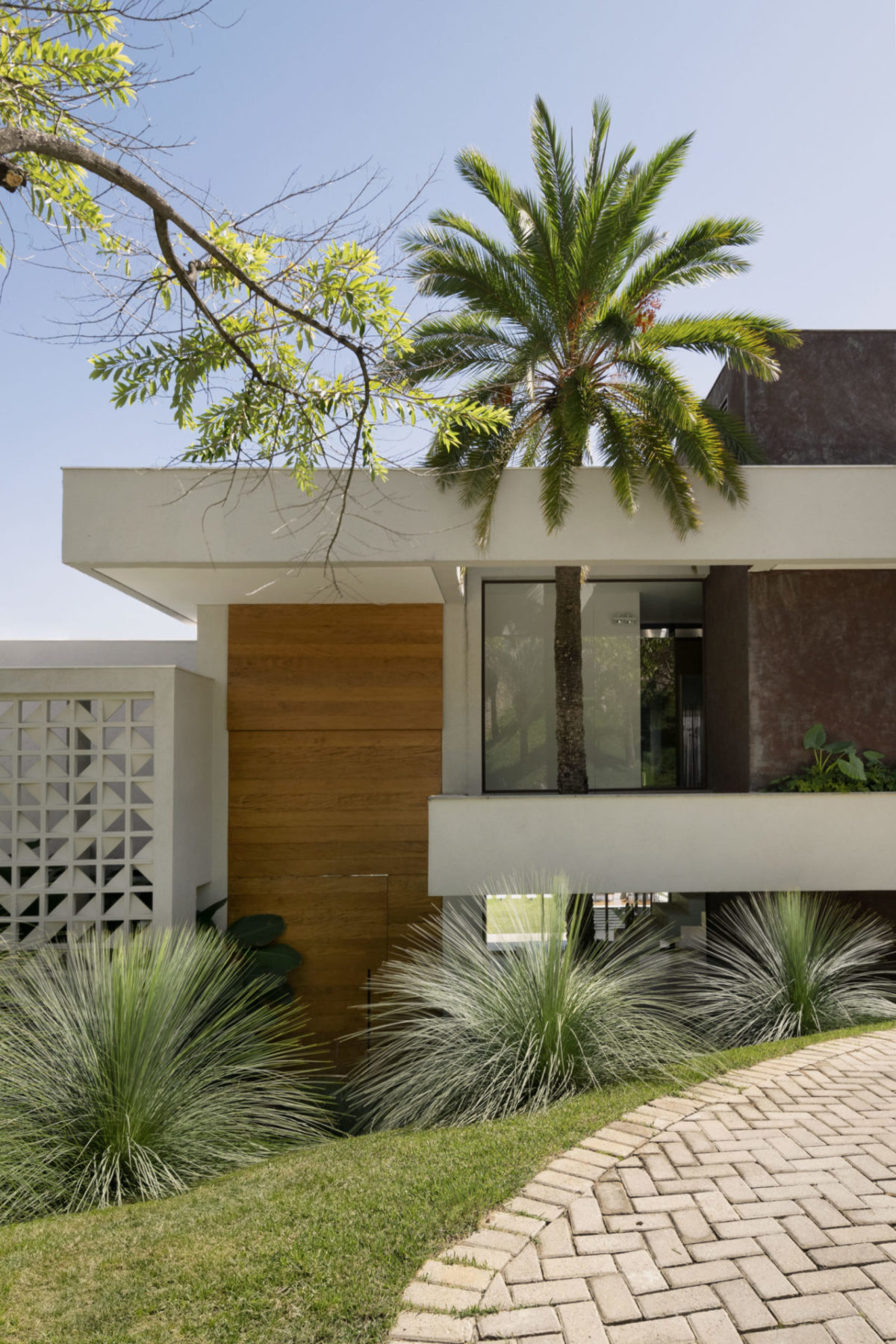 Jardim tropical e integrado à arquitetura em uma casa mineira, com o paisagismo desenvolvido em paralelo à construção, tirando partido do terreno em declive e abraçando a residência em Nova Lima, Minas Gerais.