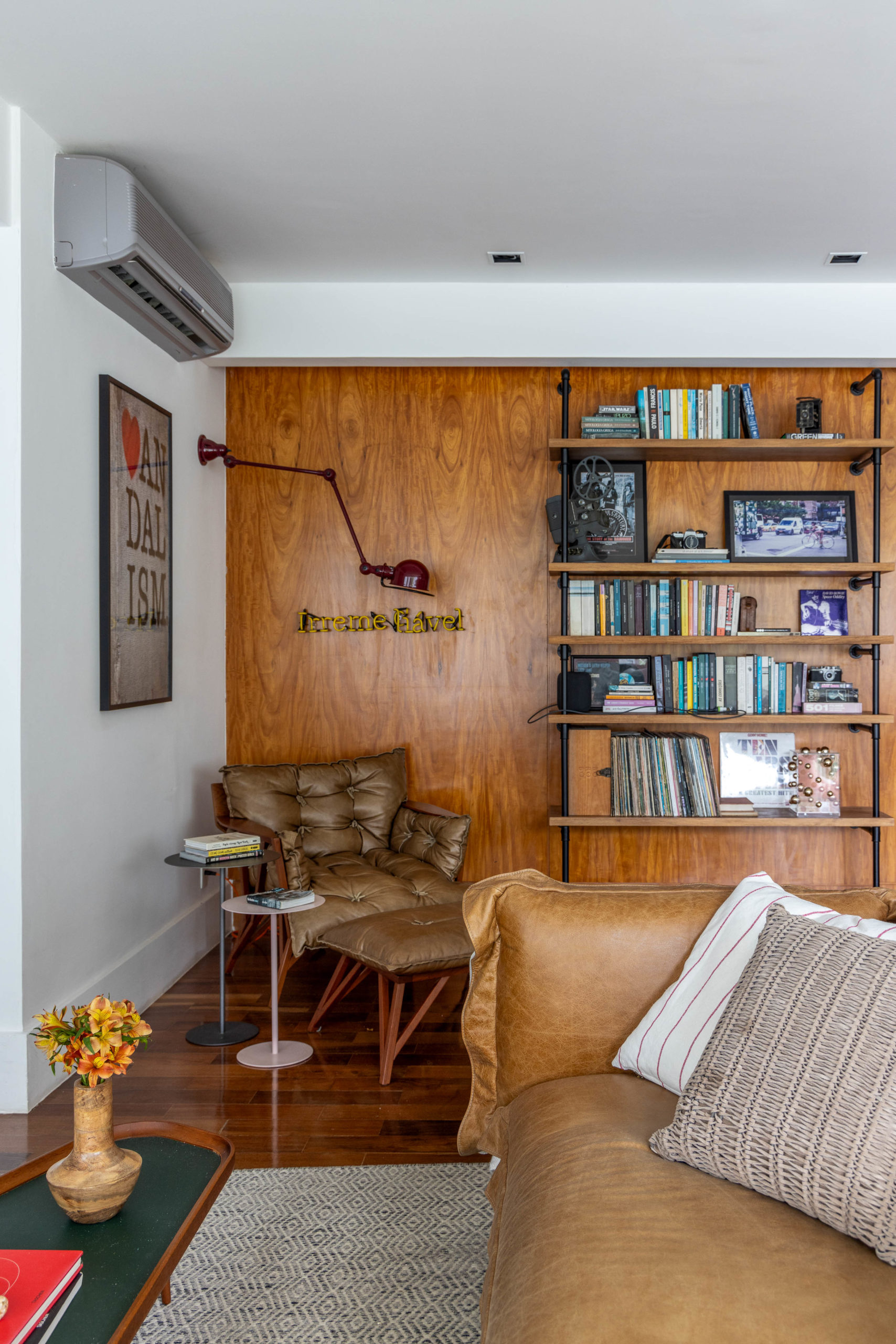 Apartamento na Gávea reflete a personalidade criativa e artística de um casal de advogados descolados, com três filhos. cantinho de leitura, composto pela poltrona Gilberto (do Paulo Alves), a luminária de parede com de luz de neon e a estante de marcenaria com prateleiras apoiadas em canos hidráulicos.