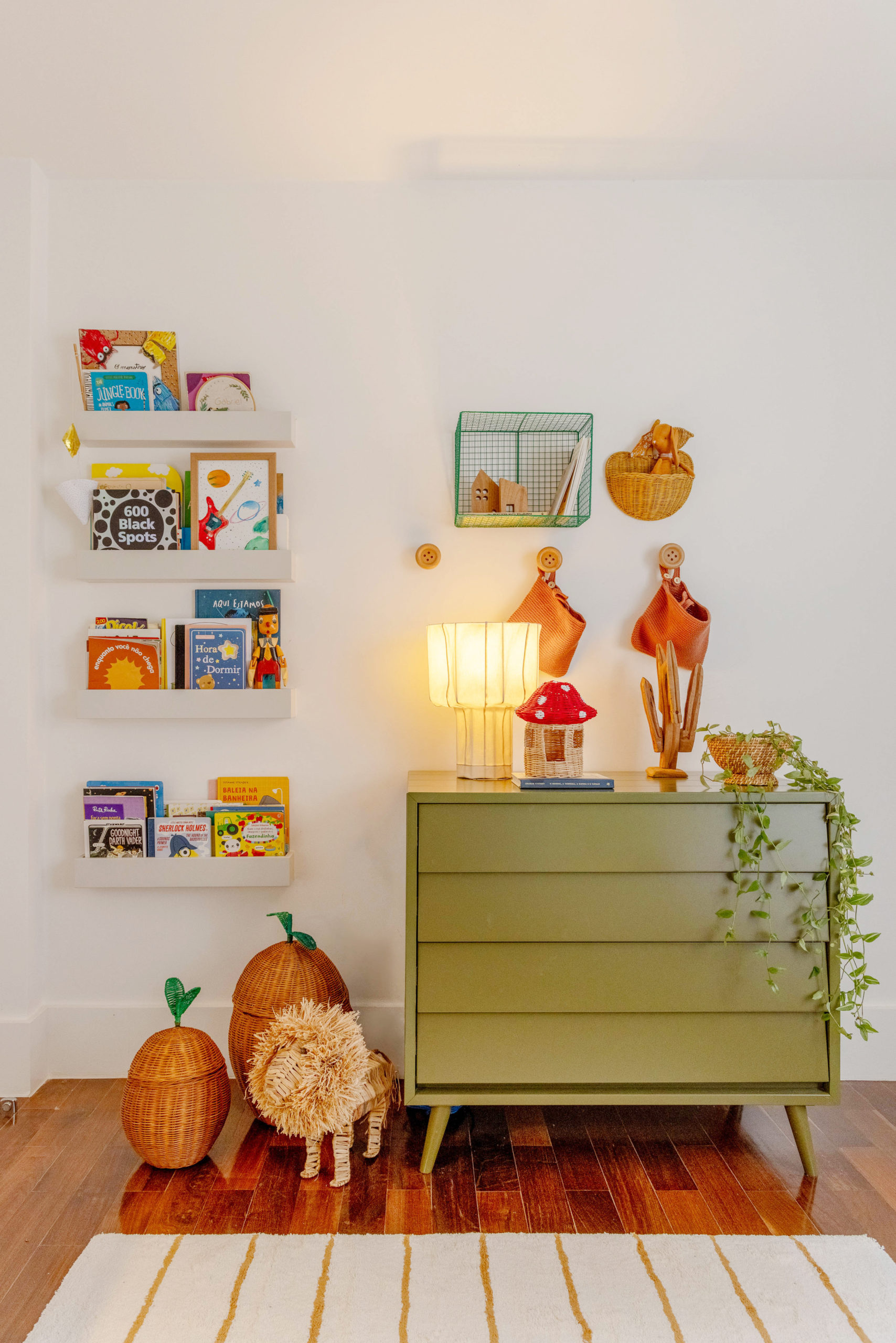 Detalhe de decoração em um quarto infantil. Comoda verde, ao lado na parede, um revisteiro.