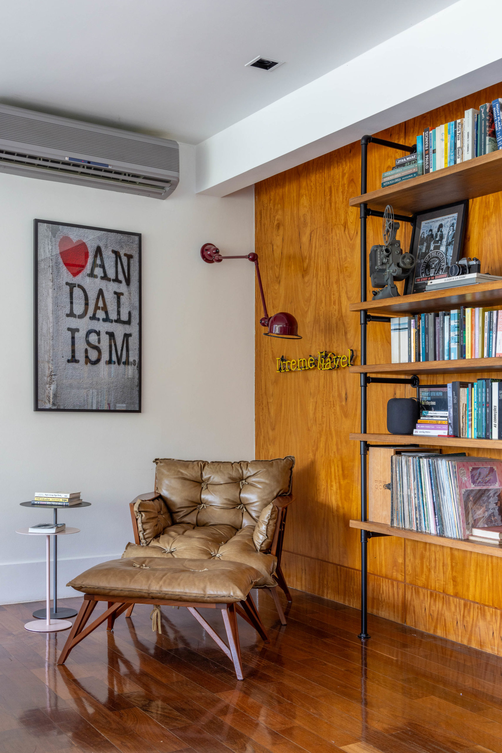 Apartamento na Gávea reflete a personalidade criativa e artística de um casal de advogados descolados, com três filhos. cantinho de leitura, composto pela poltrona Gilberto (do Paulo Alves), a luminária de parede com de luz de neon e a estante de marcenaria com prateleiras apoiadas em canos hidráulicos.