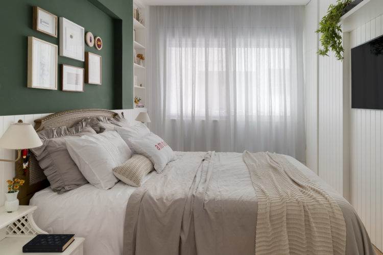 Quarto de casal com decoração estilo romântica. Cabeceira da cama em palhinha, enxoval da cama em linho bege com babados nas fronhas. Na parede da cama; meia parede em lambri branco e para cima, pintada de verde escuro.