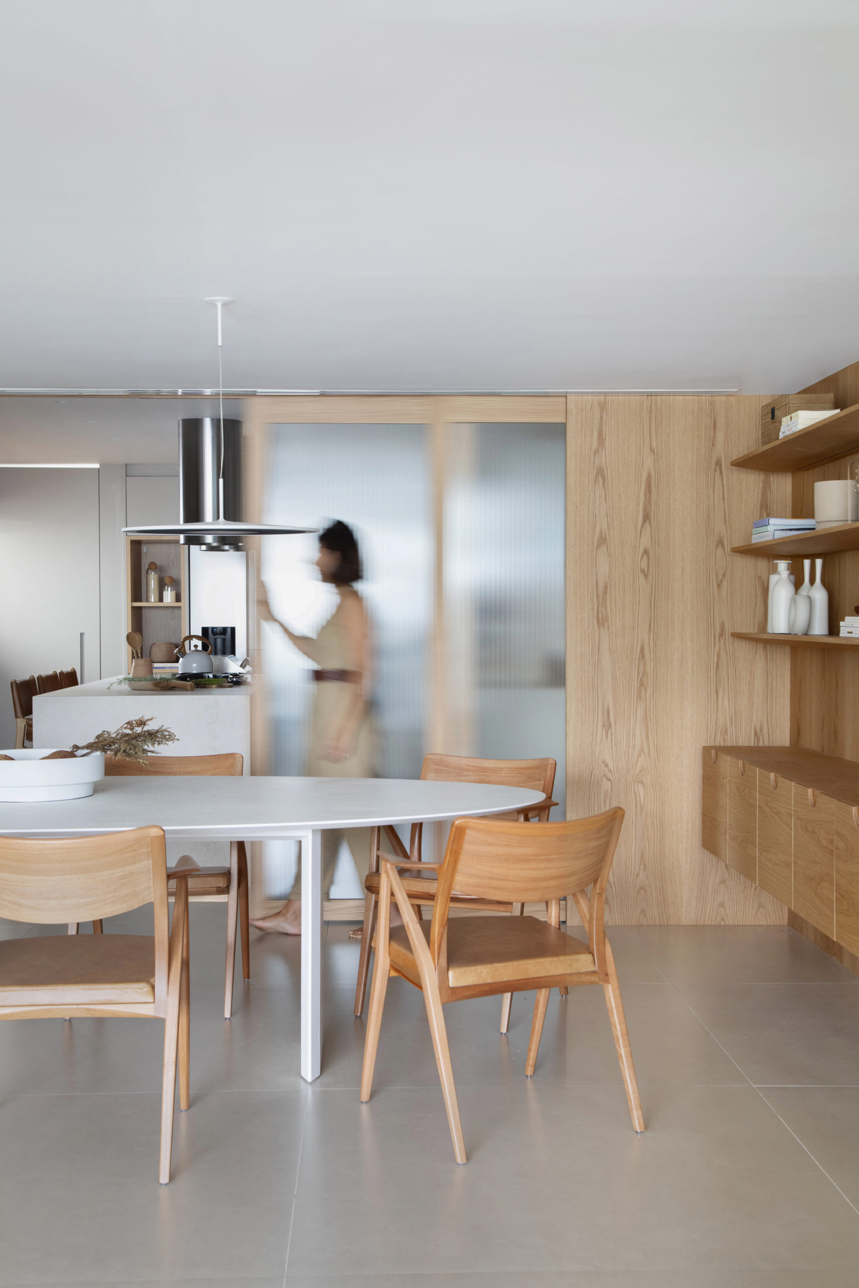 Ambiente de sala de jantar, com porta de correr que permite a integração da cozinha, quando abertas, e em madeira com vidro canelado. Marcenaria em carvalho natural na parede revestida e no aparador.