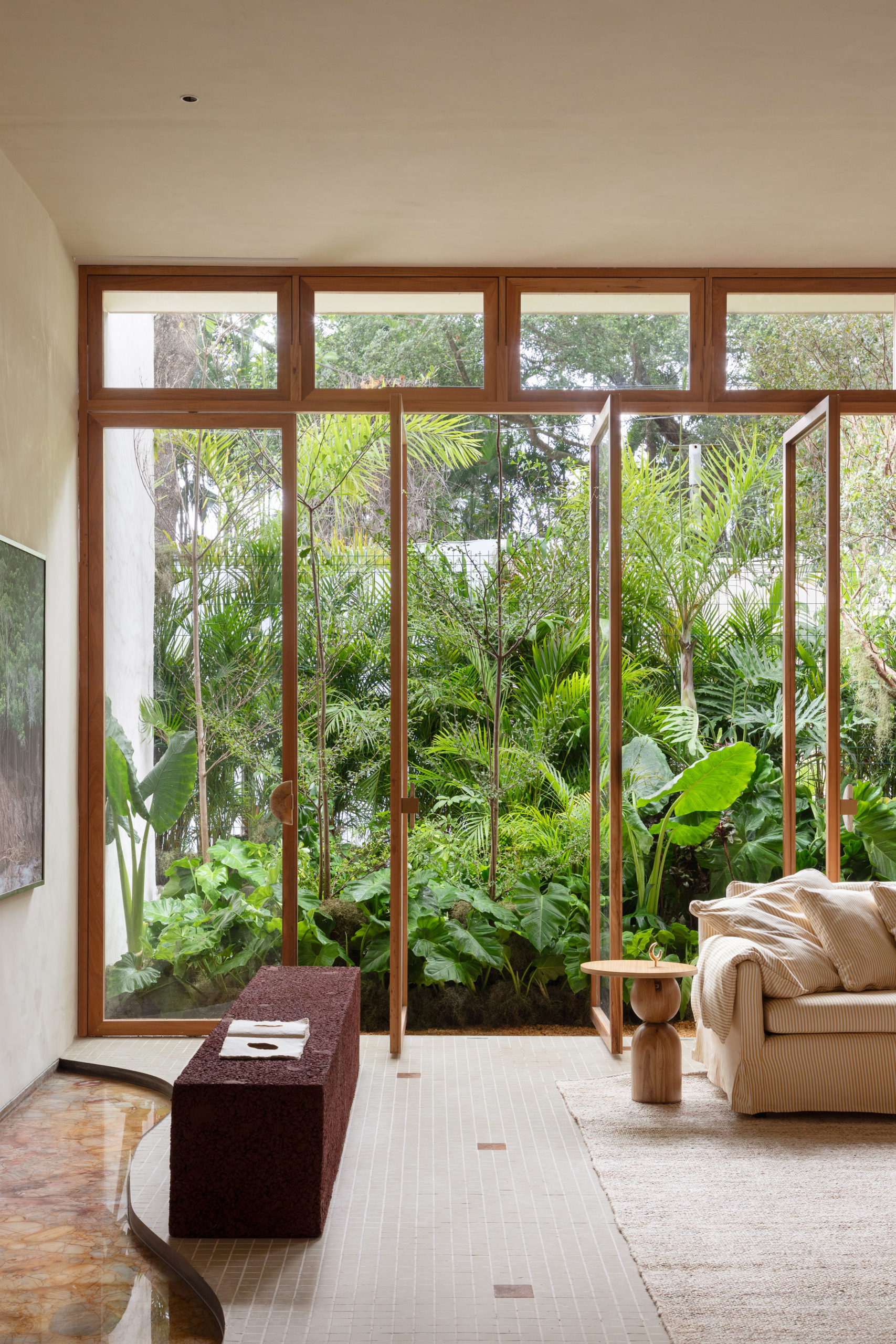 Ambiente da mostra CASACOR RIO 2024 da PKA Arquitetura. Vão com esquadrias de madeira do piso ao teto e portas em vidro, dão para o jardim.