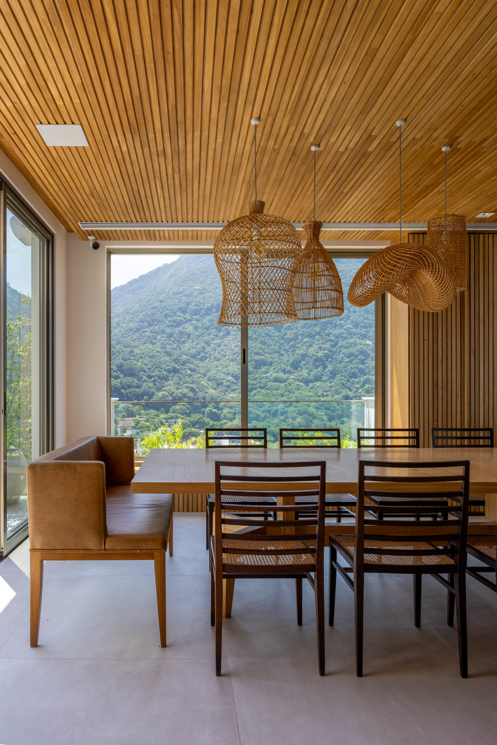 Espaço de sala de jantar, com grandes vãos de janela, com vista para o verde de São Conrado.