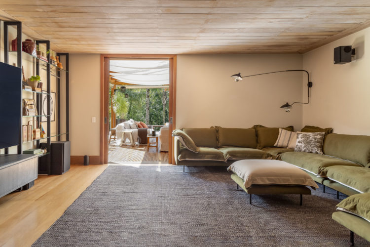 Sala de tv, com um grande sofá estofado de verde, em uma casa serrana no rio.