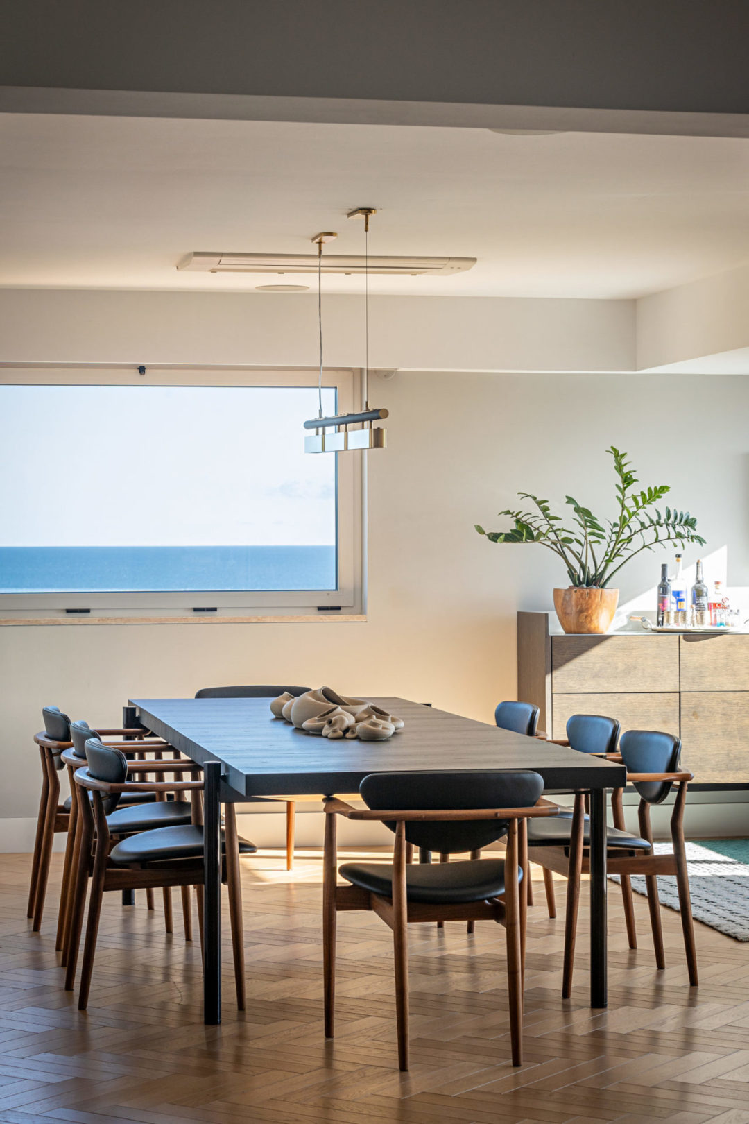 Ambiente de sala de jantar, com a mesa de tempo escuro e as cadeiras de couro preto.