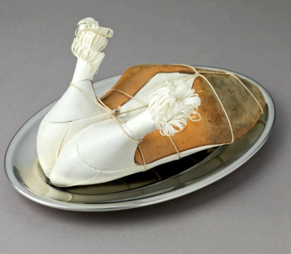 Quatro mulheres surreais. Meret Oppenheim, obra" My Nurse". Trabalho surrealista; dois sapatos amarrados de cabeça para baixo, dando a ideia de um frango assado, com as pontas do salto enfeitadas 