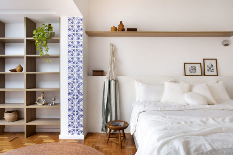 Quarto de casal, com o enxoval da cama em linho branco, uma rede na lateral da cama, uma faixa de azulejos banco e azul ao lado da estante.