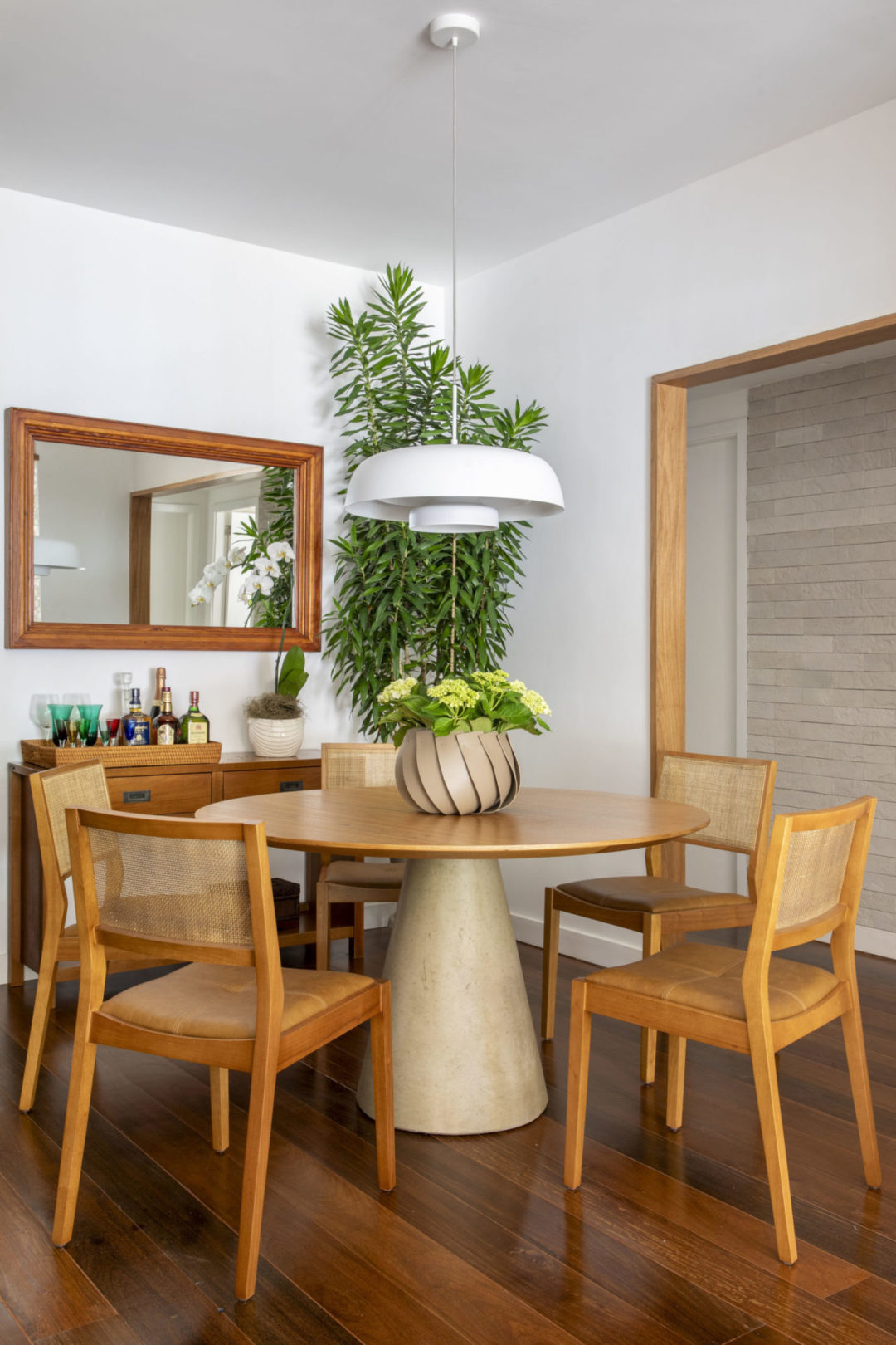 Espaço da sala de jantar, com mesa redonda com tampa em madeira e pé central em cimento.