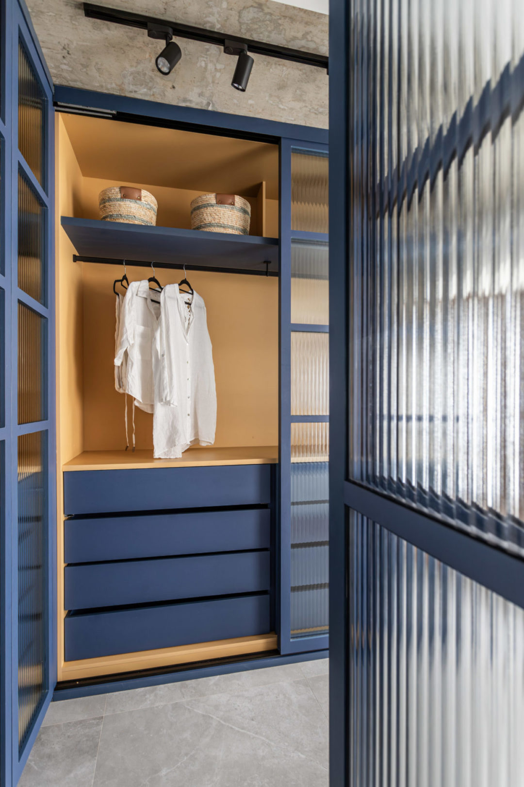 Armário de um closet: Dento do armario está na cor amarela, gavetas e estrutura do armário pintada na cor azul e os vidros canelados na porta