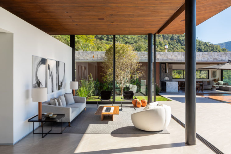 Esta casa, na serra de Petrópolis, foi construída a partir de uma estrutura metálica aparente pintada de preto, com forro do teto em ripas de Pinus tonalizado e fachadas ora em esquadrias piso-teto de alumínio preto e vidro transparente (que permitem integrar os espaços internos com a área externa) ora em painéis articulados de alumínio ripado com pintura amadeirada, ora em pedra Moledo.