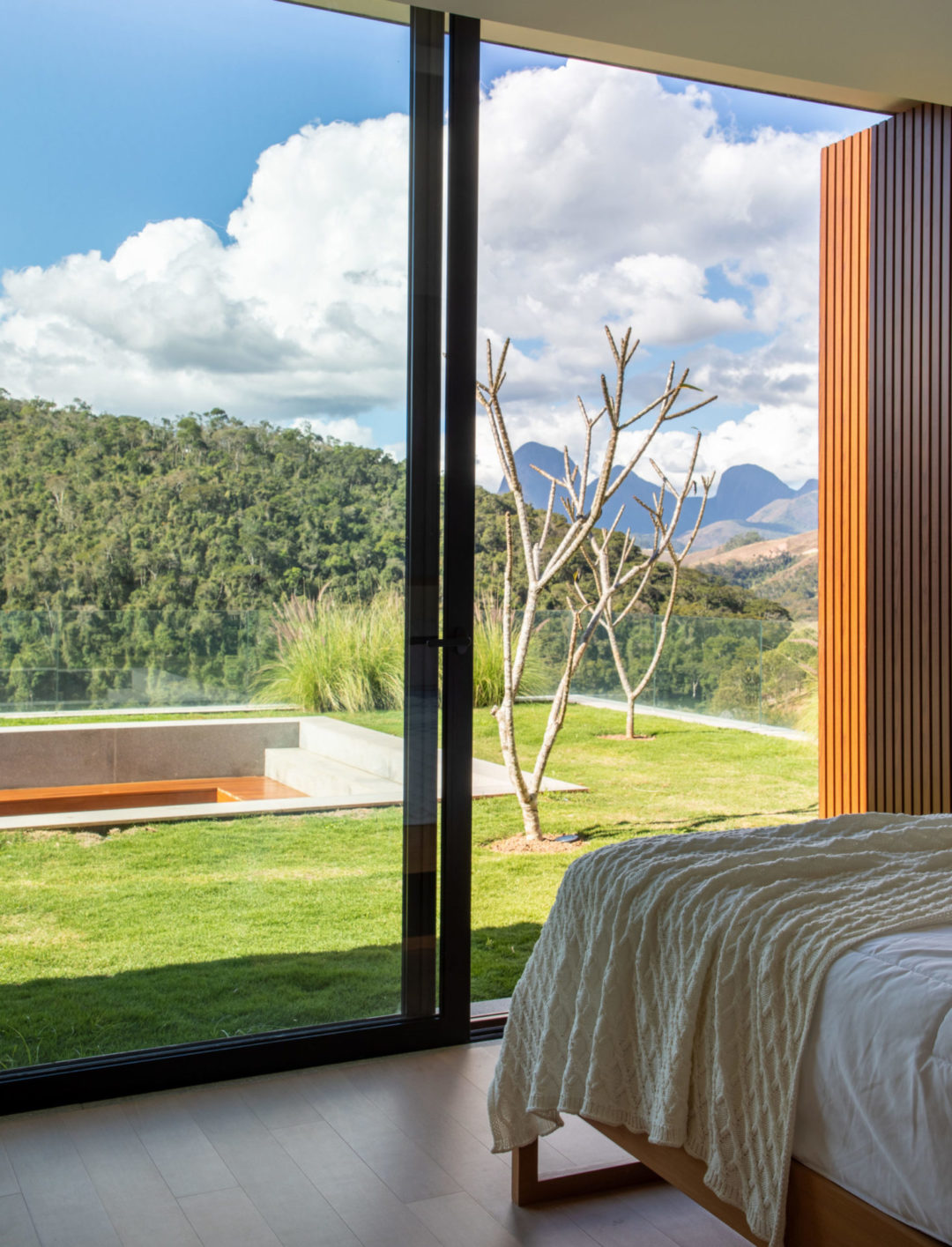 Quarto em uma casa na serra Fluminense, em itaipava, tem a cama de frente para a janela com vistas para as montanhas.