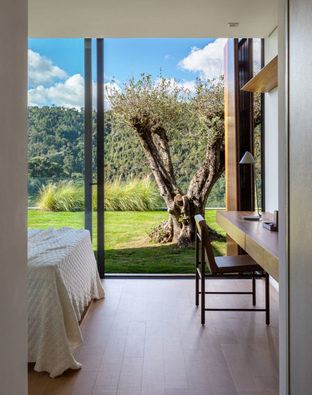 Quarto em uma casa na serra de Petrópolis, com portas de vidro de piso o teto, com vista para as montanhas.