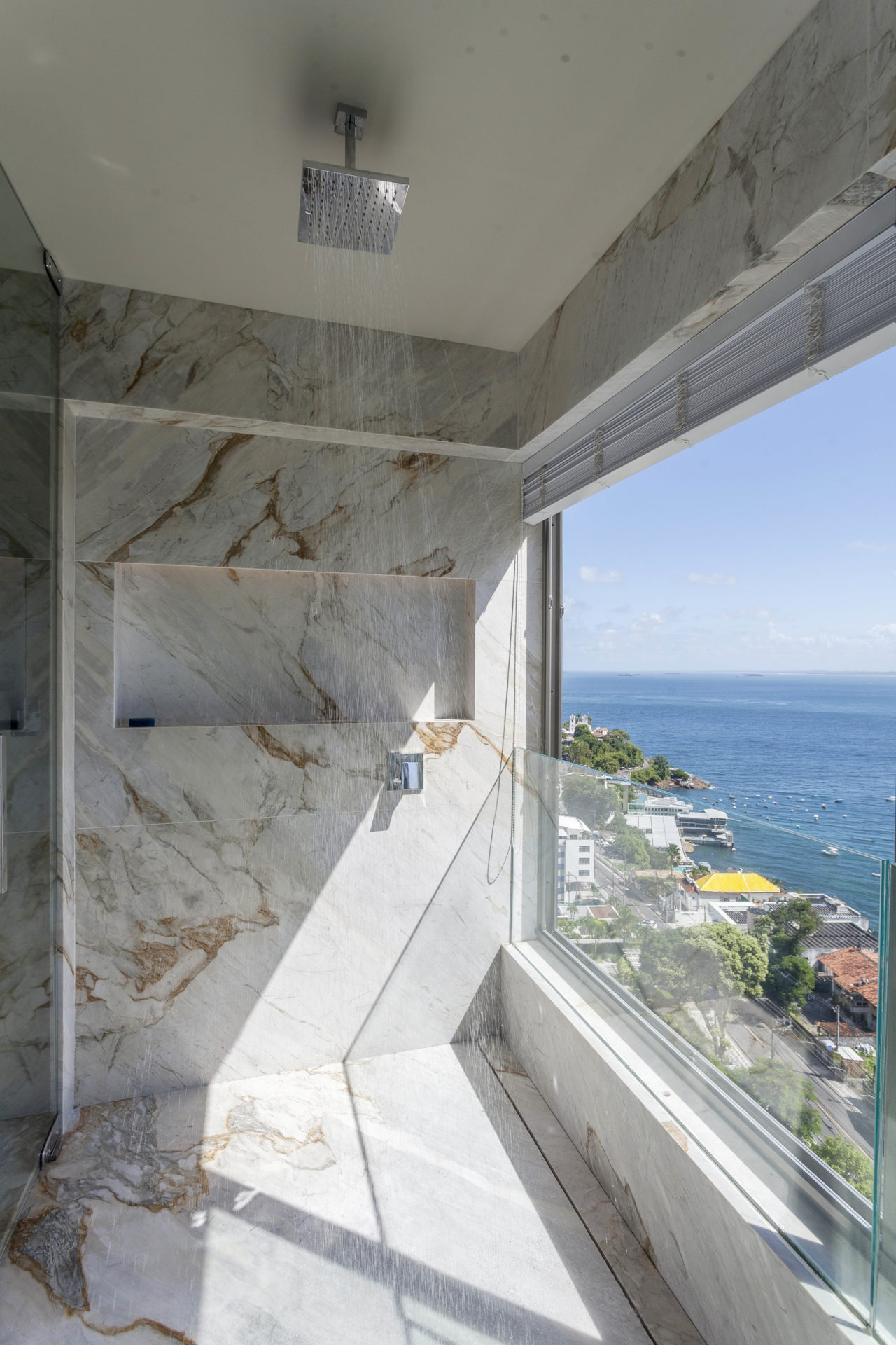 Um incrível box todo revestido em mármore, com chuveiro do teto e um janelão em vidro com a vista debruçada sobre a baia de todos os santos, Salvador