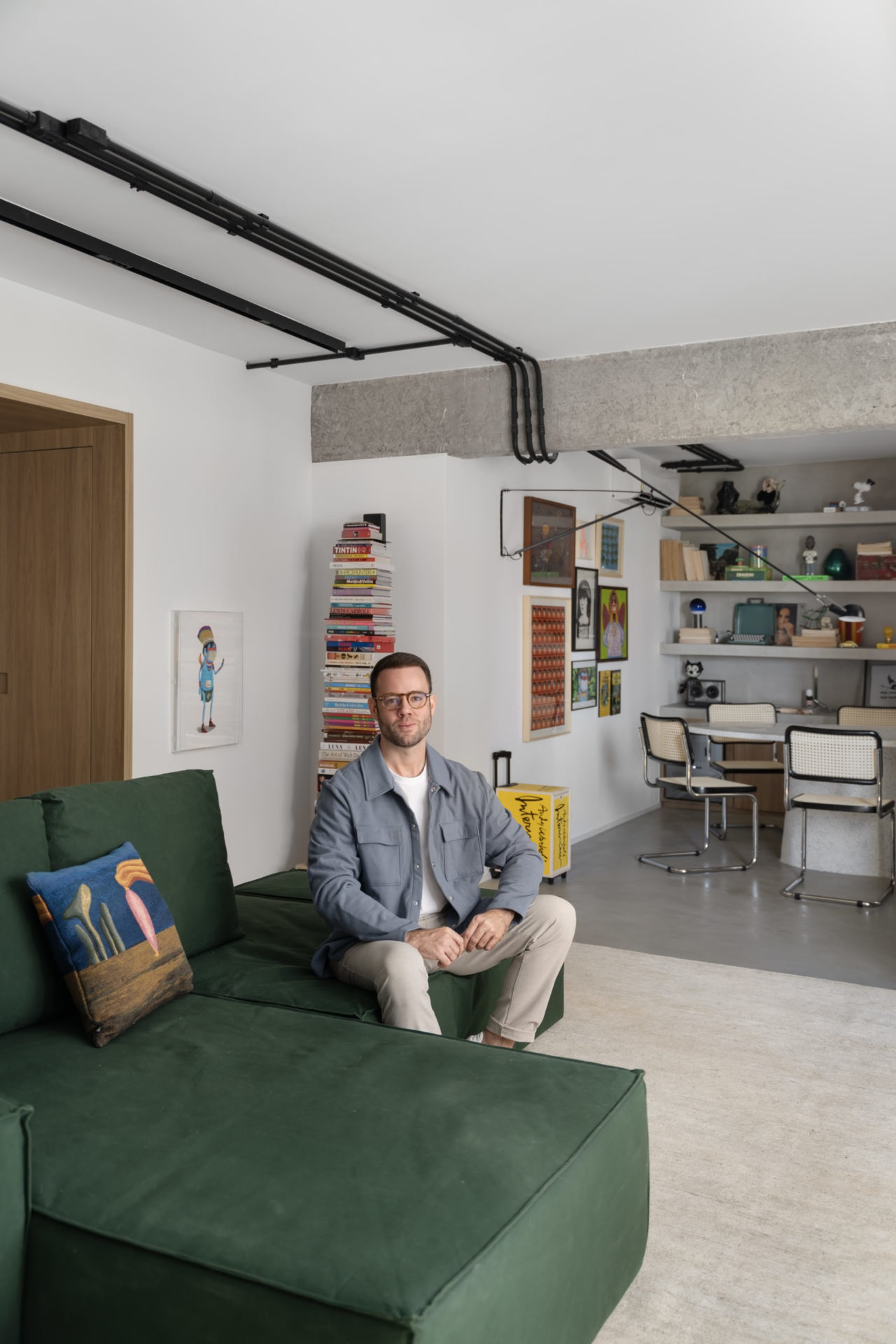 Proprietário do apartamento sentado em um sofá numa sala com visual clean e industrial