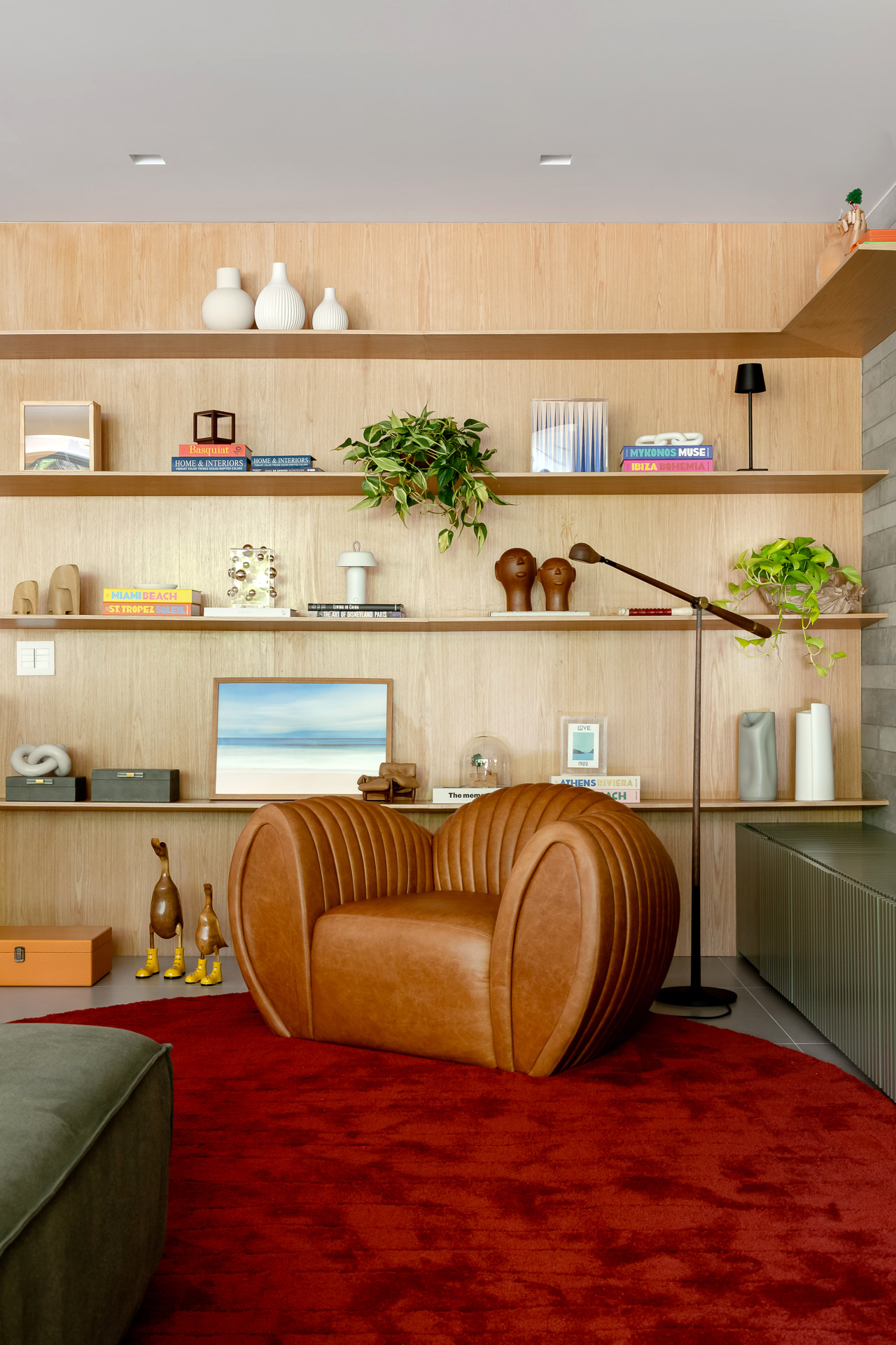 sala com tapete vermelho, poltrona de couro e estante na parede