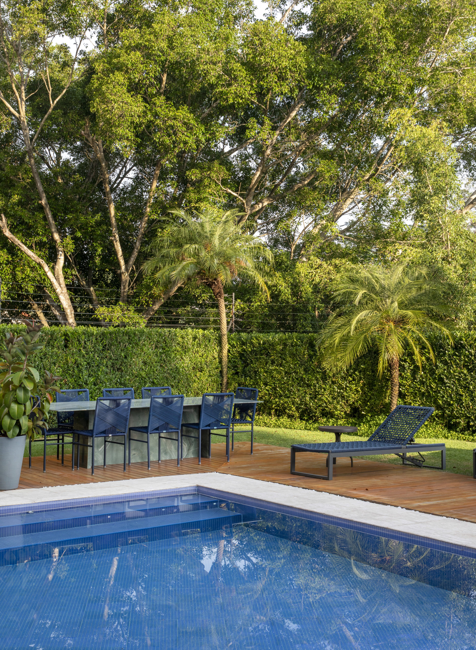 piscina em área verde com uma mesa com 8 cadeiras e uma espreguiçadeira