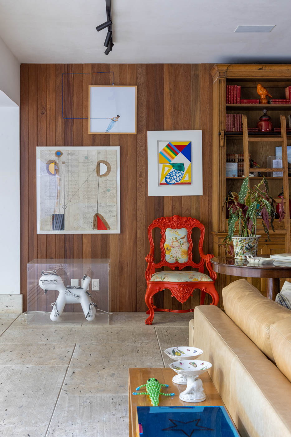 Parede com partes da coleção de arte do morador e uma cadeira vermelha.