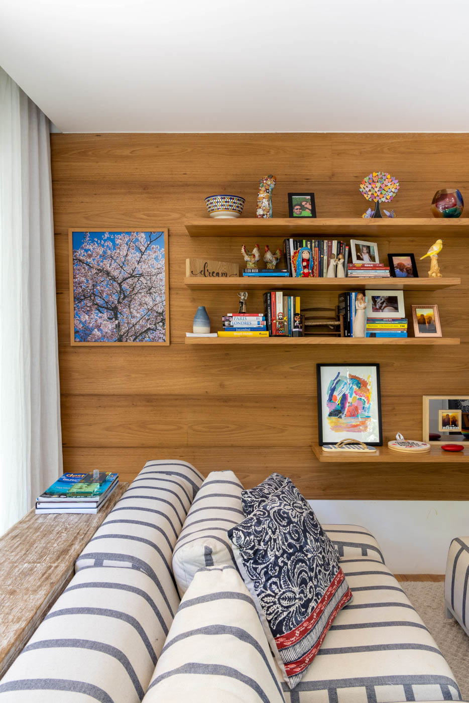 Parede revestidas em madeira, com prateleiras, também em madeira, com livros e porta retratos.