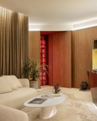 espaço com sofá branco, mesa de centro branca, cortina e parede em madeira