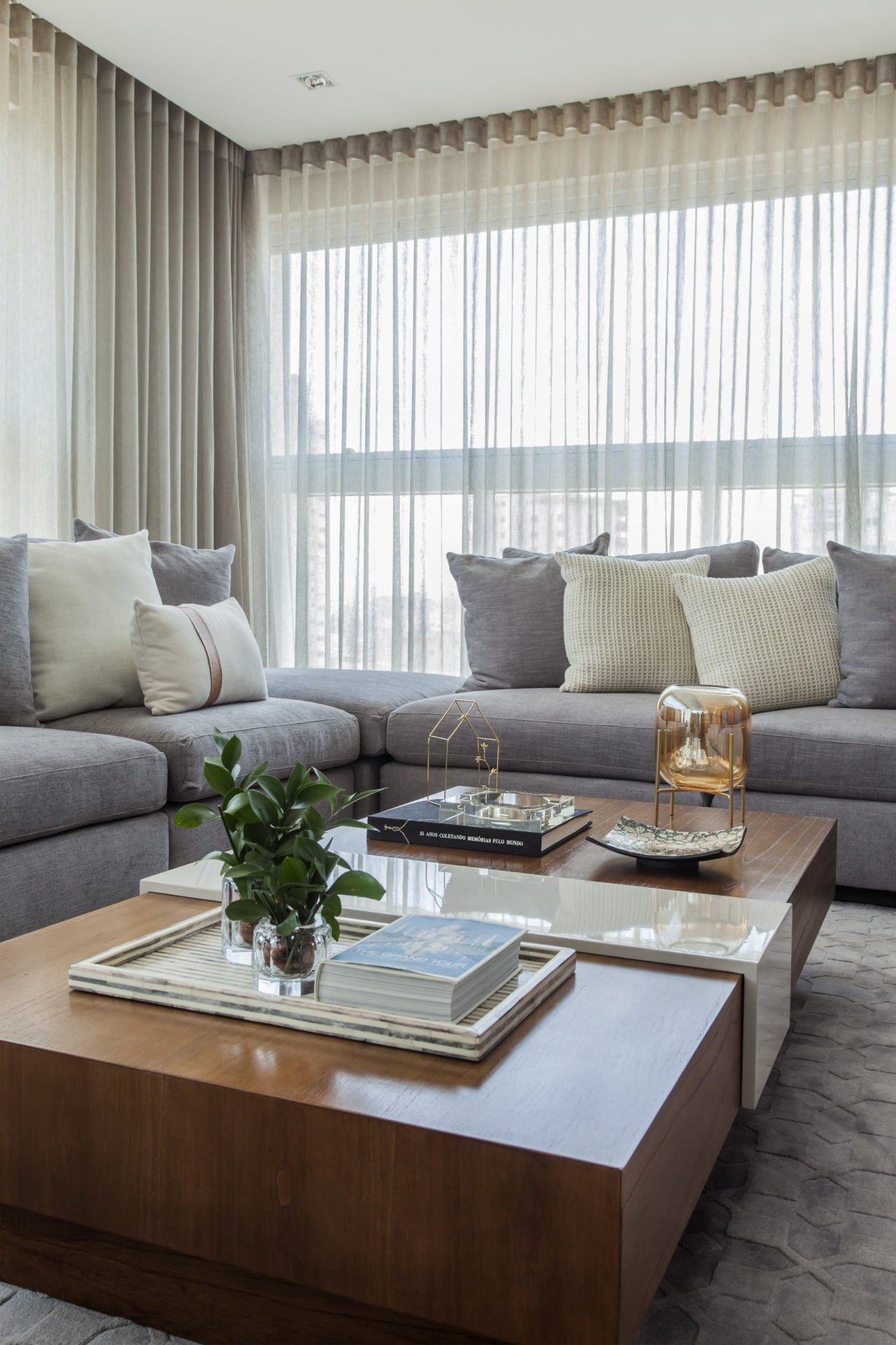 sala com cortina branca, sofás cinza, almofadas e mesa de centro quadrada