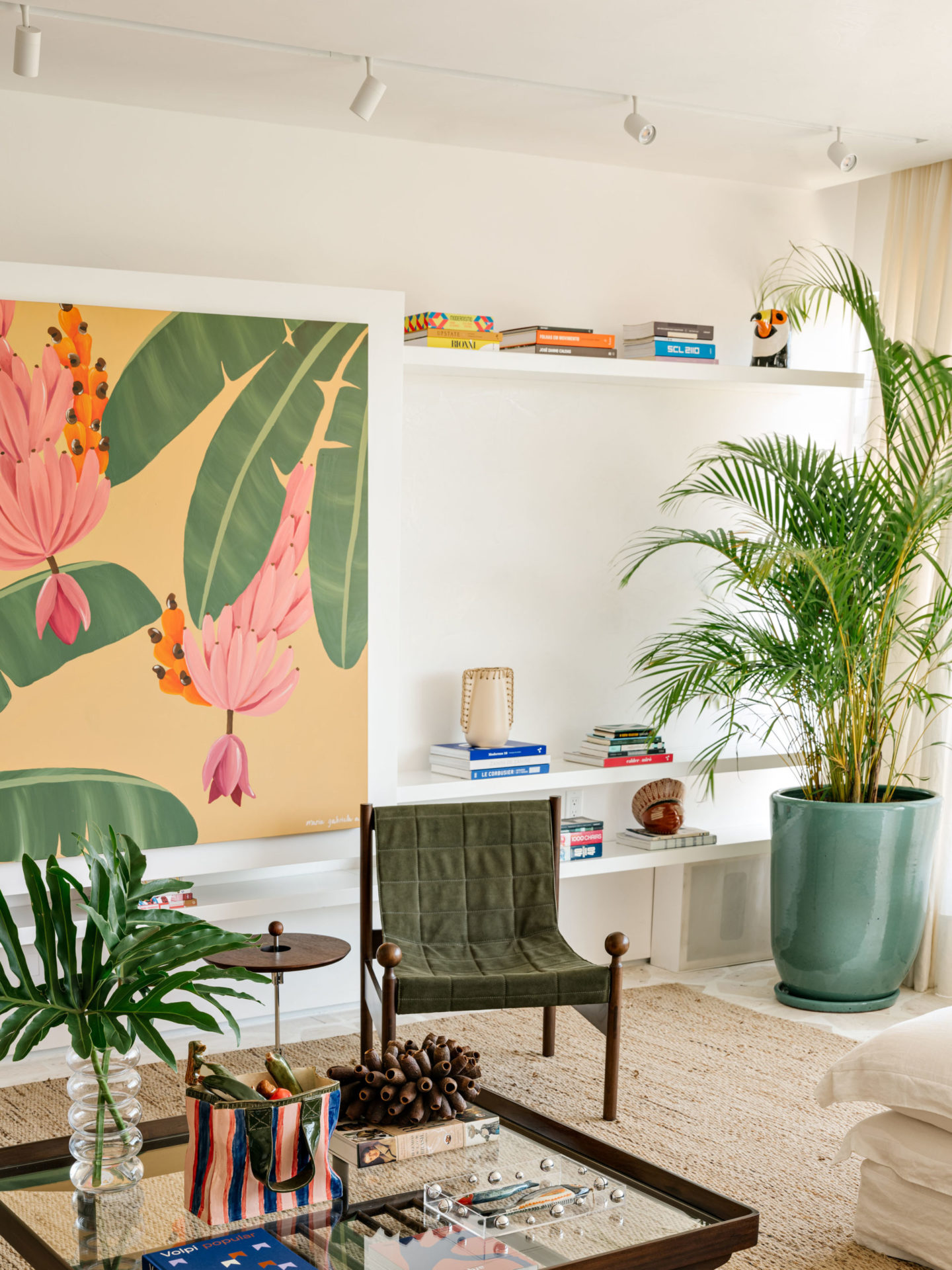 na foto imagem de uma sala com quadro de flores e plantes, uma cadeira e um vaso de plantas