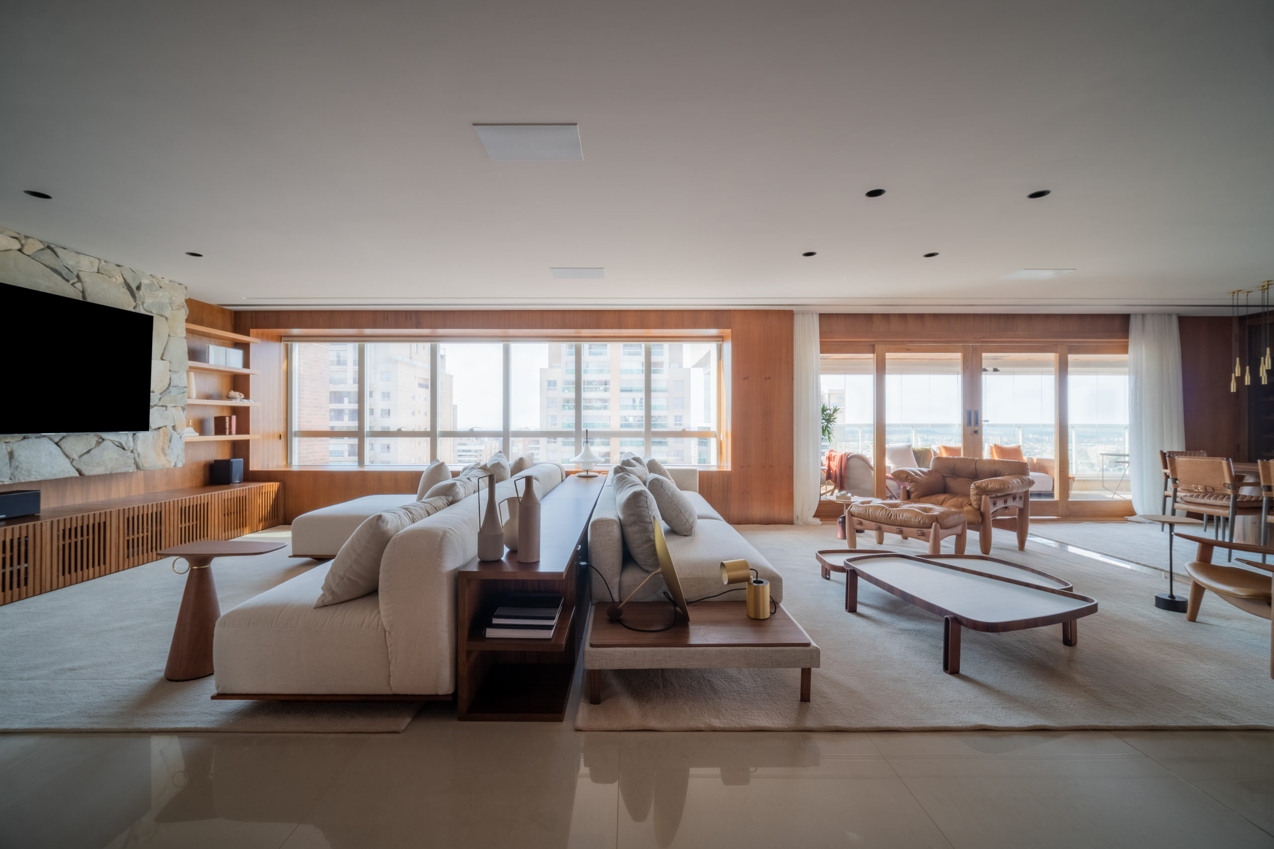 sala com duas janelas grandes, sofás, mesa de centro, TV e mesa de jantar