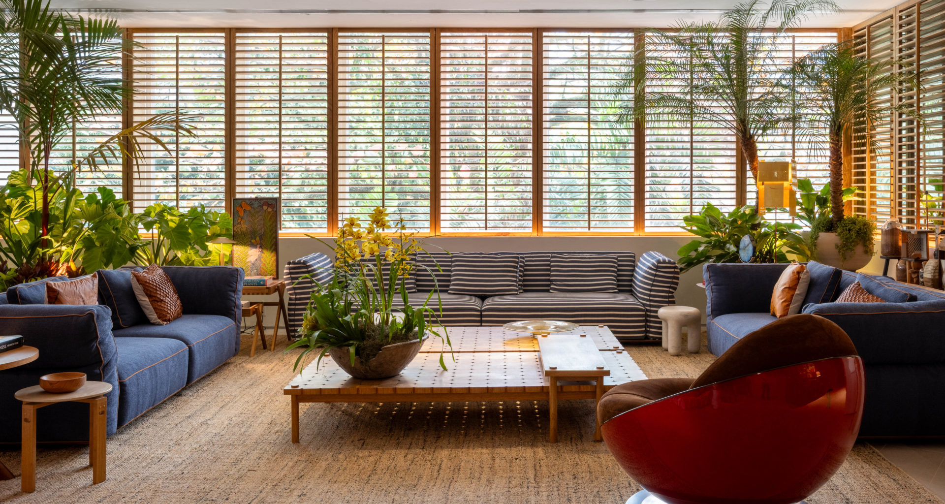 living com sofás em tom de azul, poltrona vermelha, mesa de centro e shutters de madeira