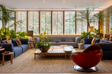 living com sofás em tom de azul, poltrona vermelha, mesa de centro e shutters de madeira