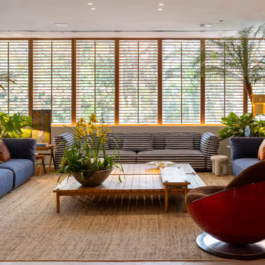 living com sofás em tom de azul, poltrona vermelha, mesa de centro e shutters de madeira