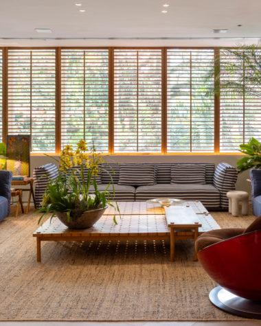 living com sofás em tom de azul, poltrona vermelha, mesa de centro e shutters de madeira