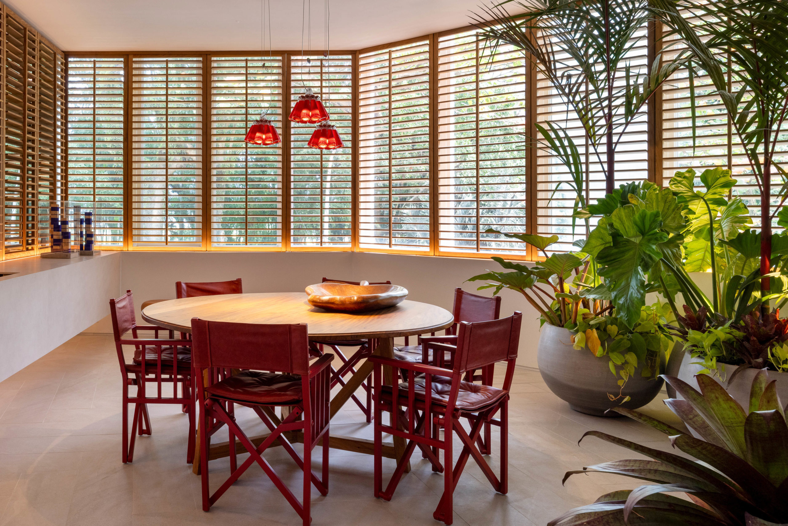 espaço com mesa de jantar, plantas e persianas de madeira