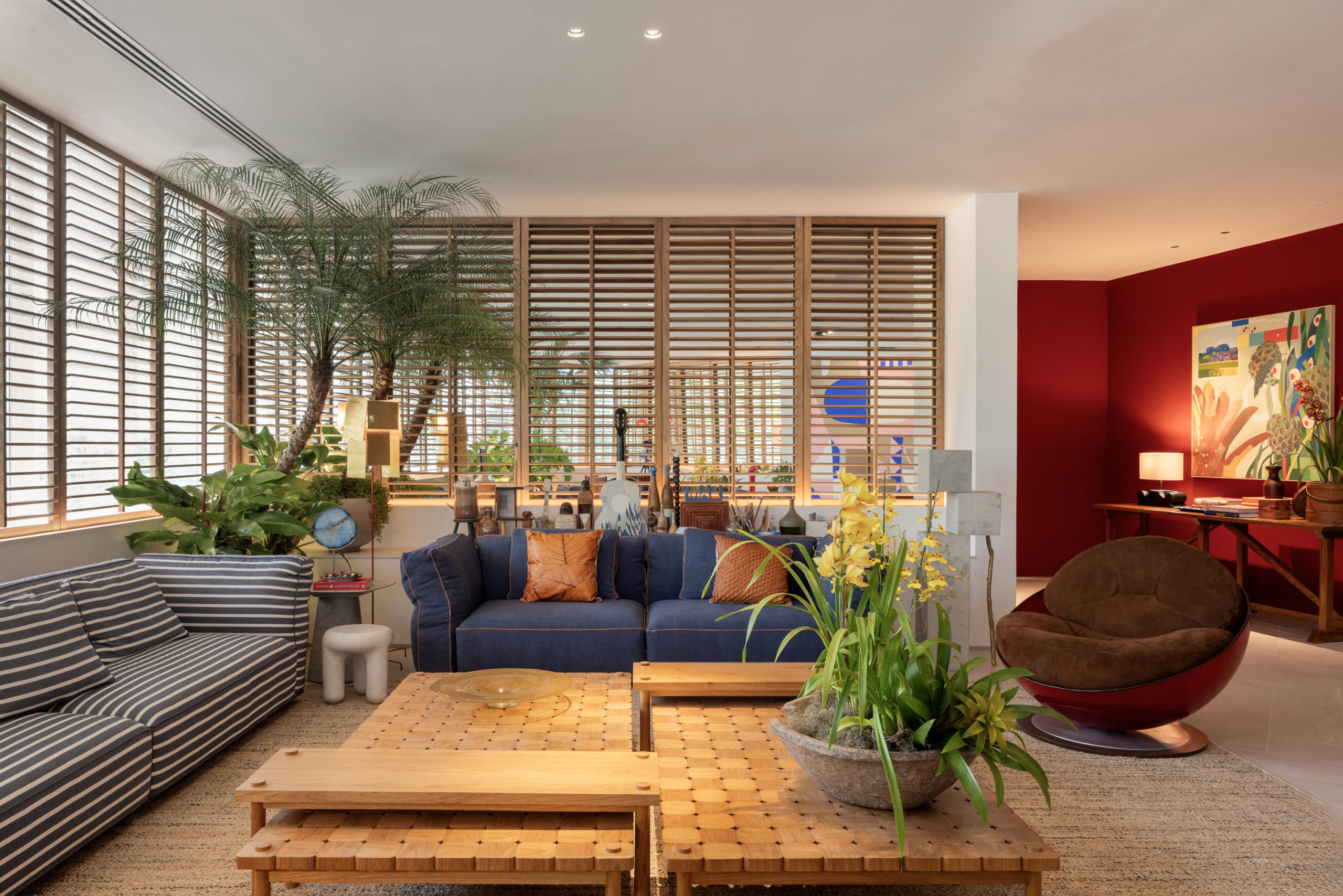 living com sofás no tom azul, plantas e shutters de madeira