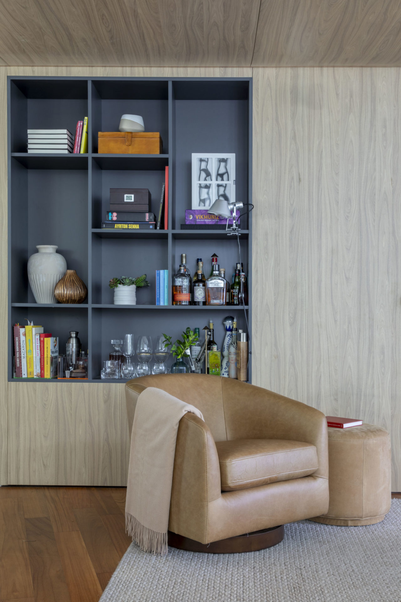 sala com poltrona na cor bege e estante embutida na parede com objetos de decoração