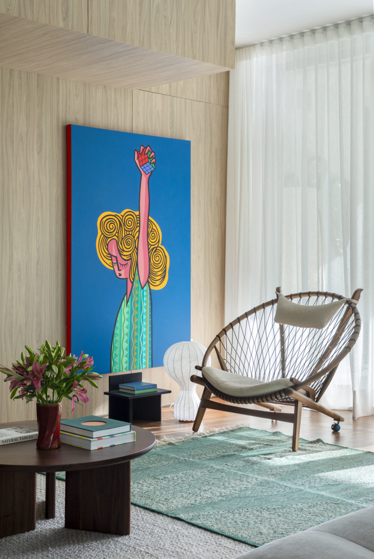 sala com poltrona, mesa de centro com flores e livros e quadro grande na parede