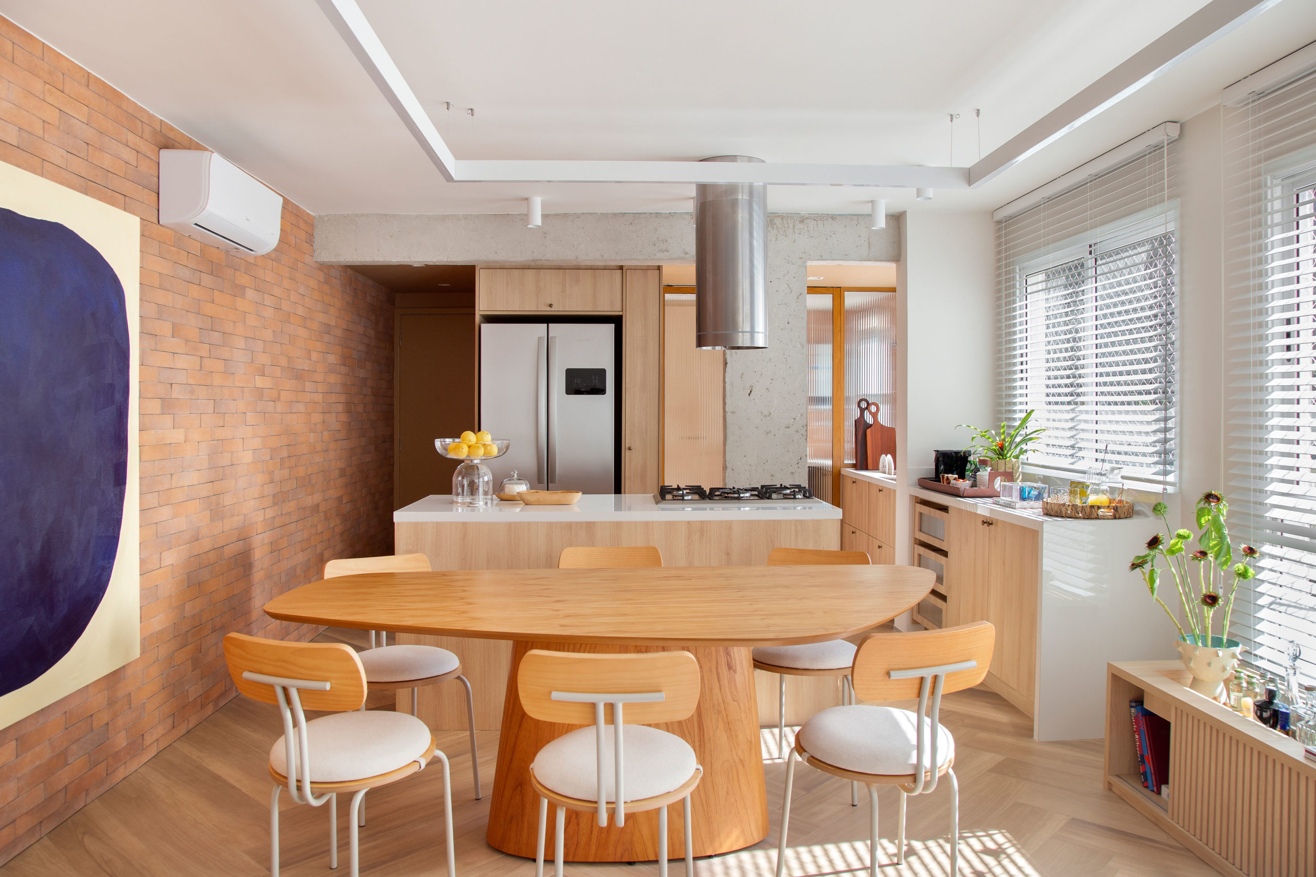 sala com parede de tijolinhos, mesa com cadeiras e cozinha ao fundo