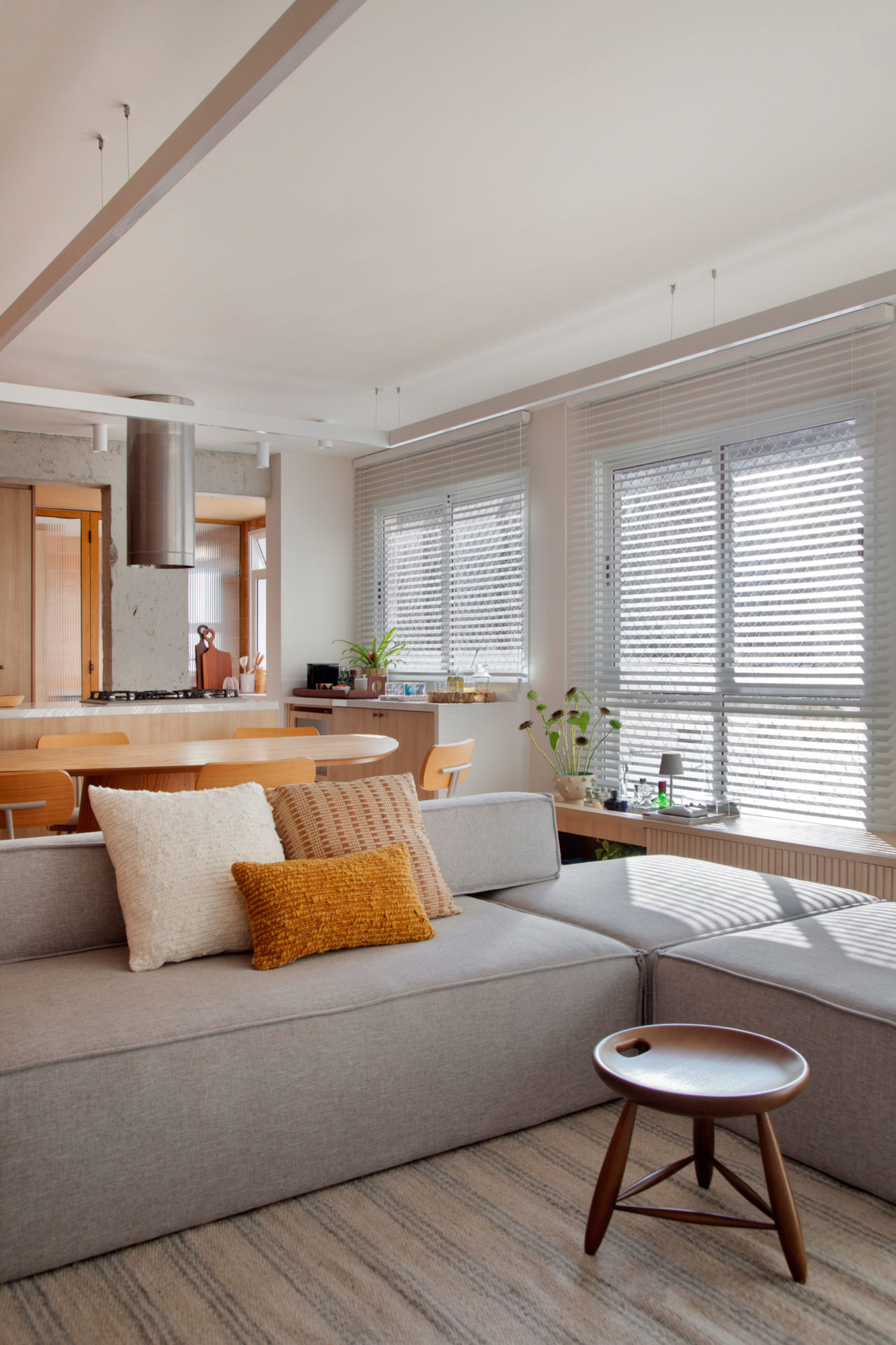 sala com forro rebaixado, sofá e vista para a cozinha. no sofá três almofadas 