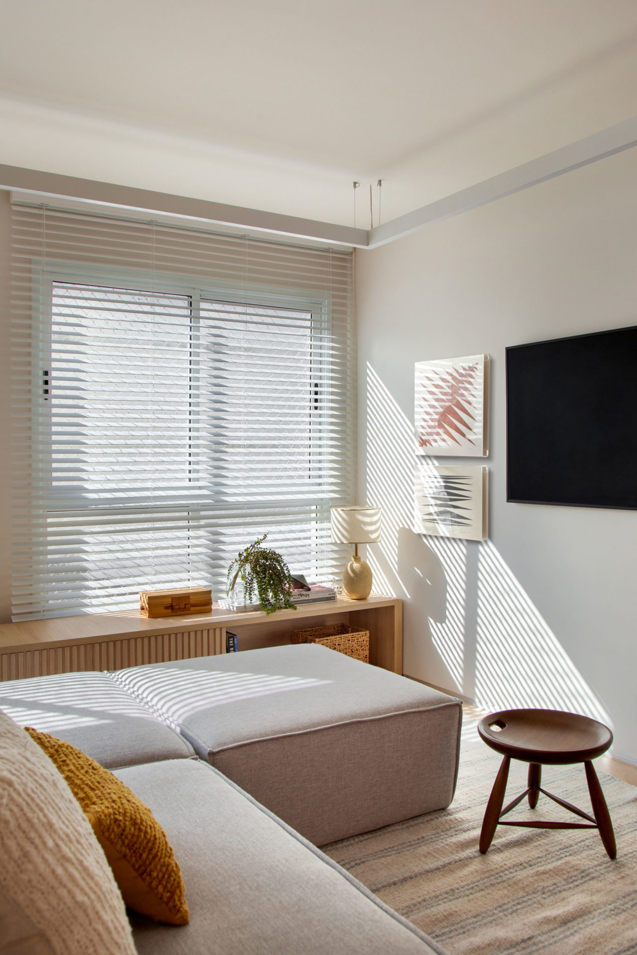 sala com sofá, janela, quadros e banquinho de madeira