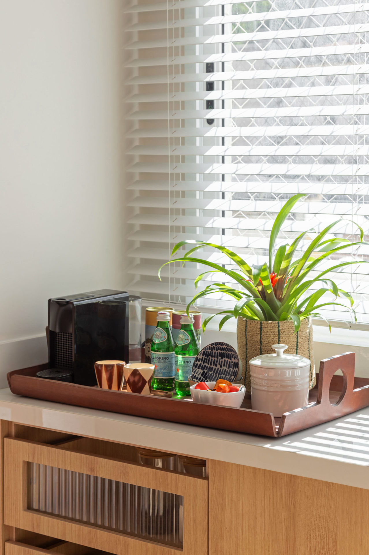 janela com persiana branca e bandeira com vaso de planta, cafeteira e garrafas de água