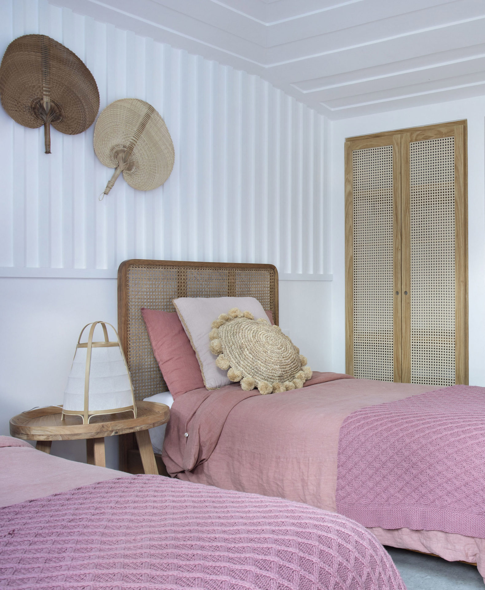 quarto de casa de praia em búzios com duas camas de solteiro e dois leques de palha na parede