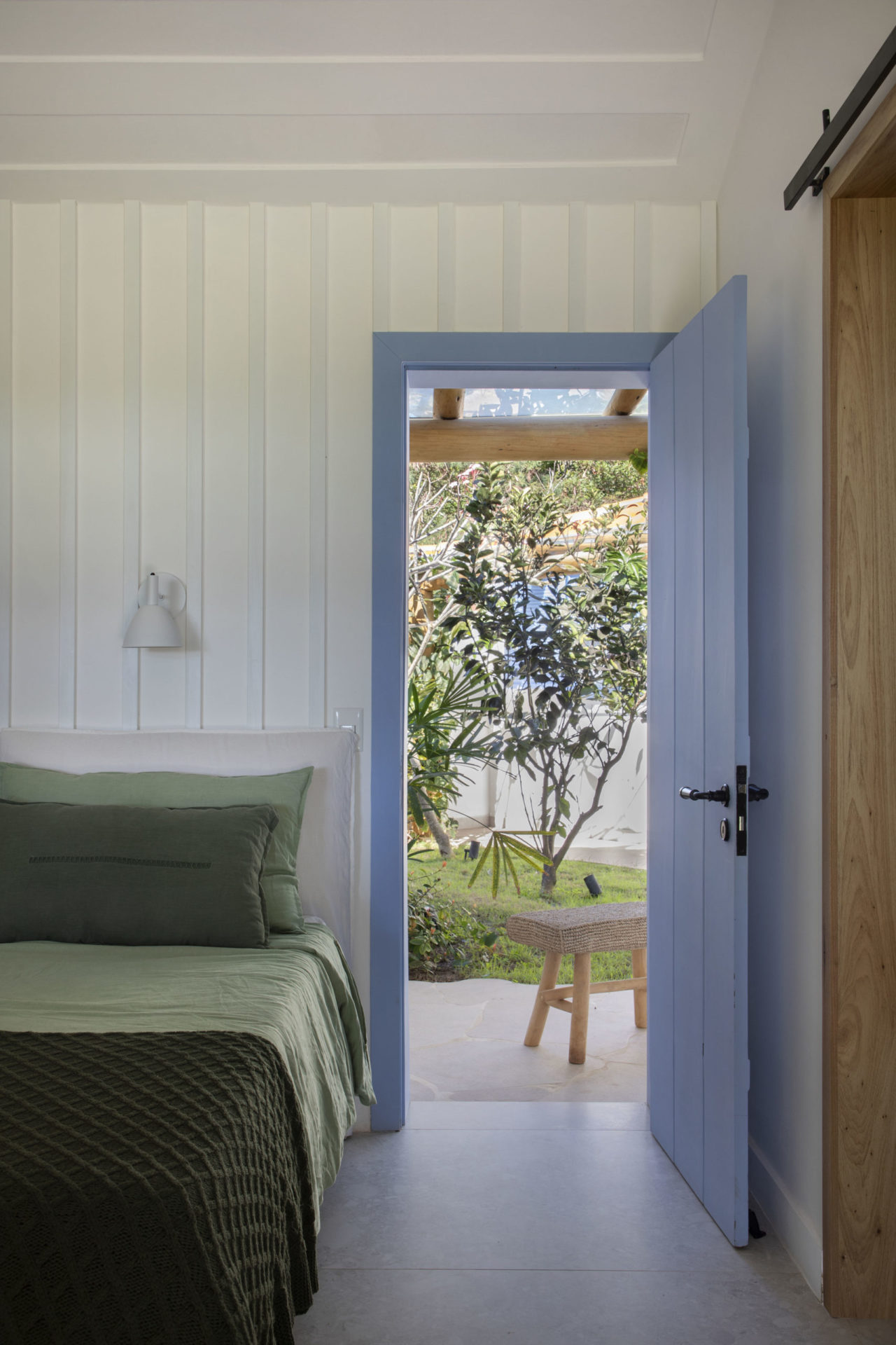 quarto com paredes brancas e porta na cor azul aberta com vista para o jardim
